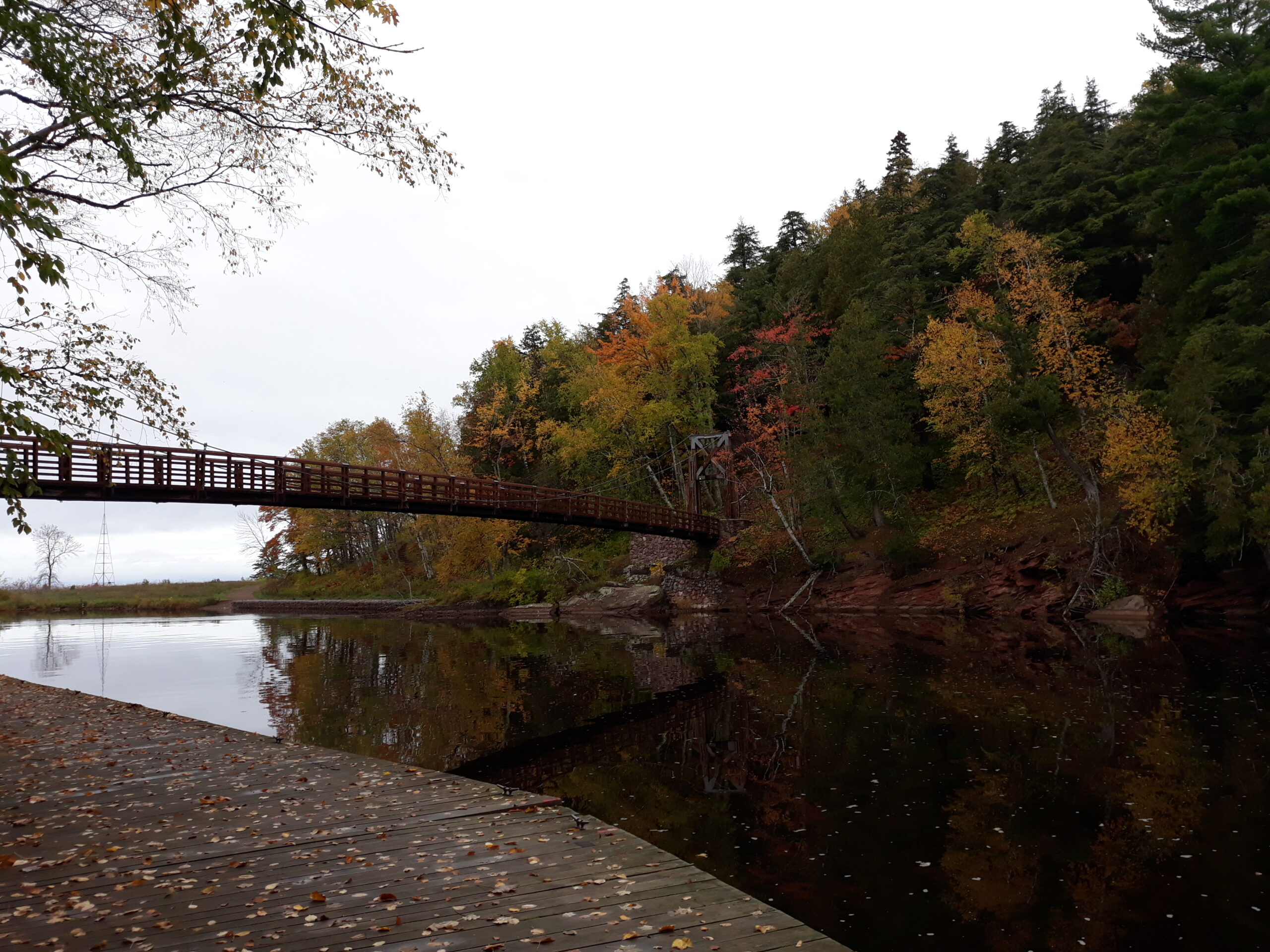 A bridge stretches over a reflective river and onto an opposite shore with bright fall colors.