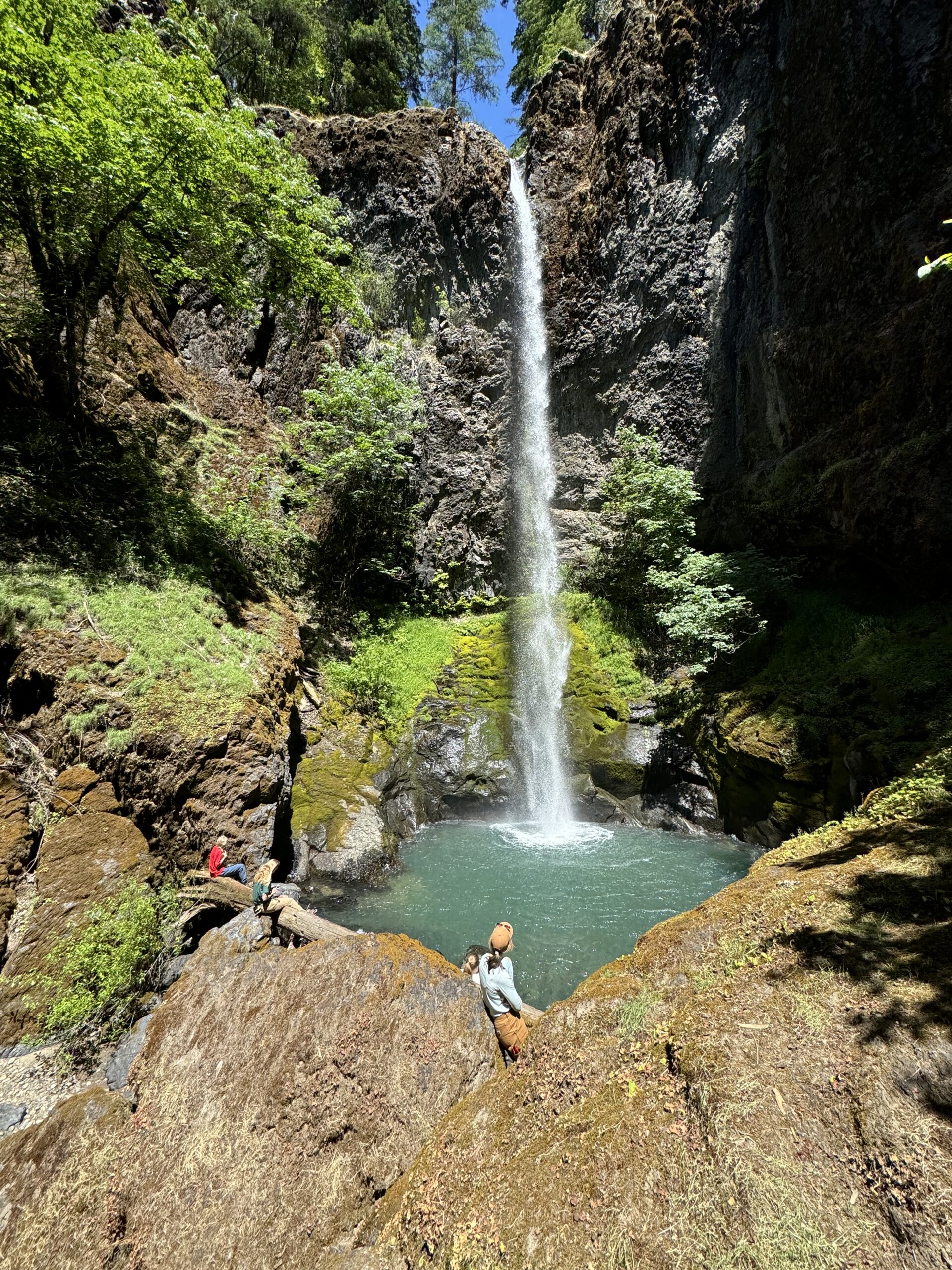 Water falls into a blue pool with people sitting on a log